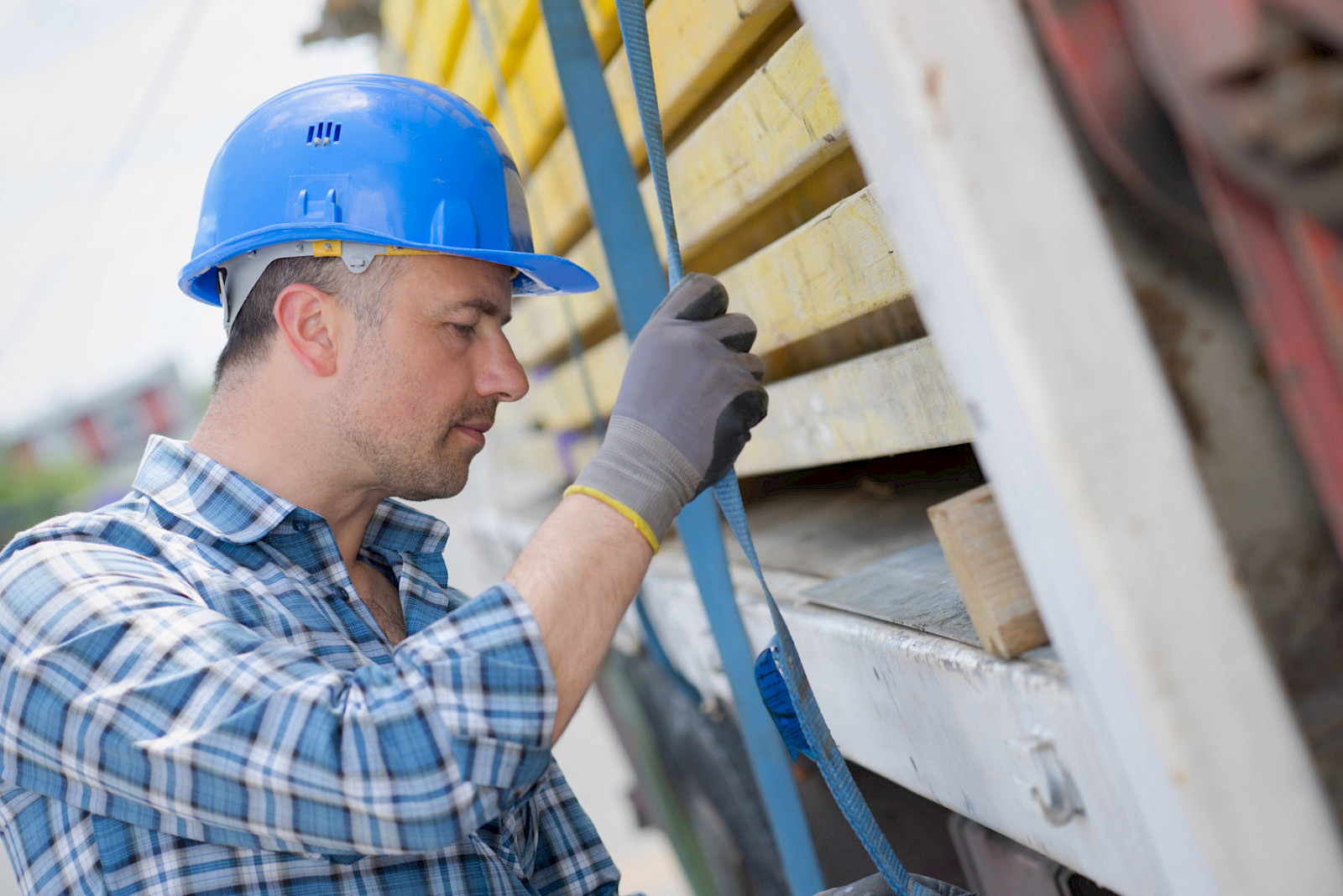 Arbeiter mit Schutzhelm sichert eine Ladung mit Spanngurten auf einem Lkw