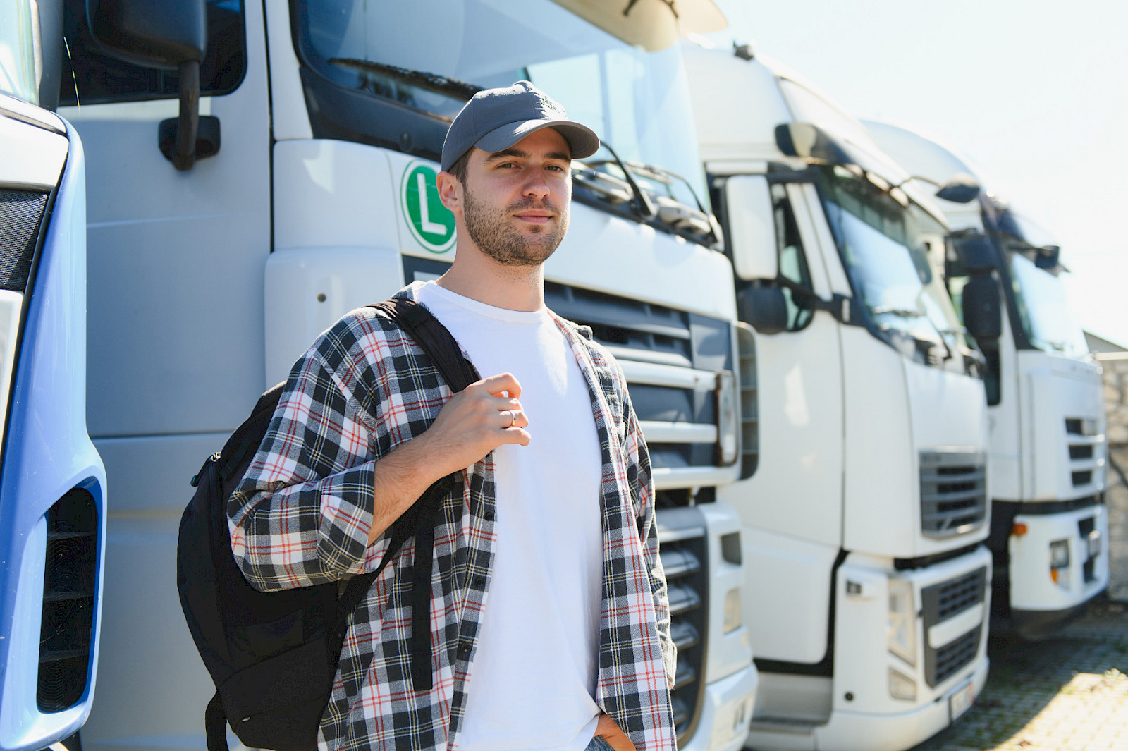 Junger angehender Lkw-Fahrer mit Rucksack vor einer Reihe Lastwagen