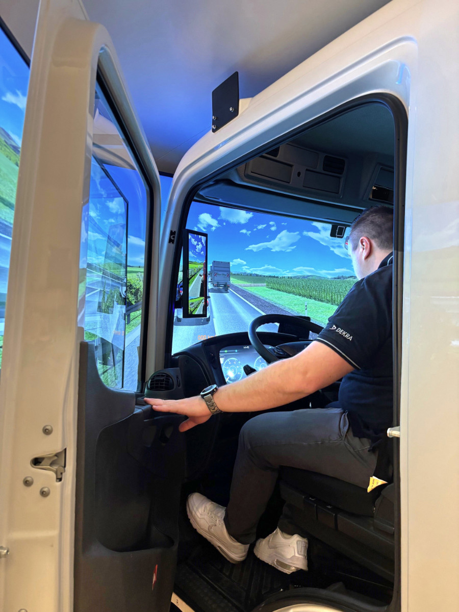 Person sitzt in einem DEKRA-Lkw-Fahrsimulator mit Stra&szlig;enansicht auf den Bildschirmen