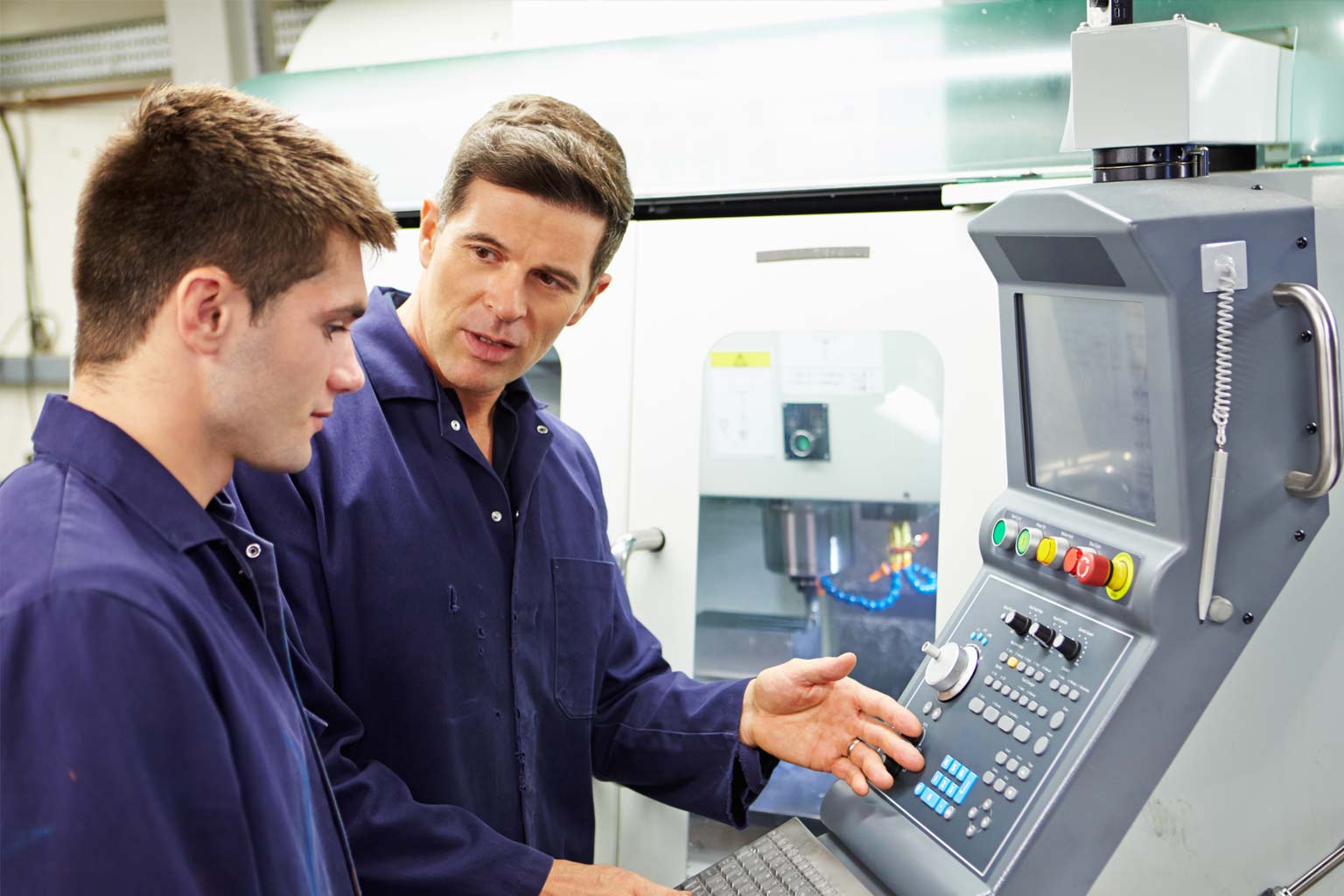 Facharbeiter weist einen jungen Auszubildenden an einer CNC-Maschine ein